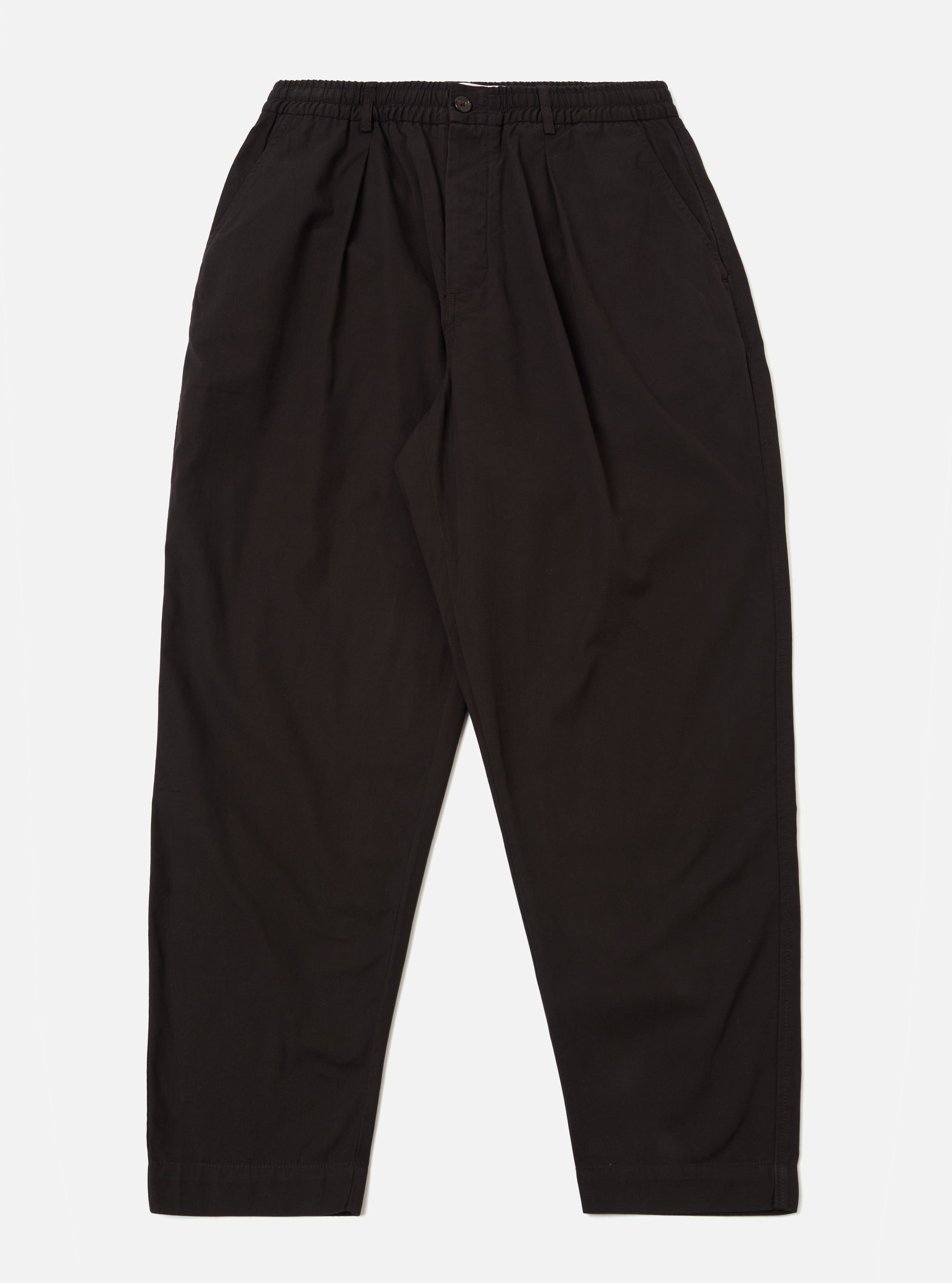 The Licorice Summer Canvas Pleated Track Pant is shown as a flat lay against a plain white background. The trousers feature an elasticated waistband with an internal drawstring, a single pleat on each leg, and a tapered silhouette. The fabric is a solid licorice brown cotton canvas with visible stitching at the hem and pockets.