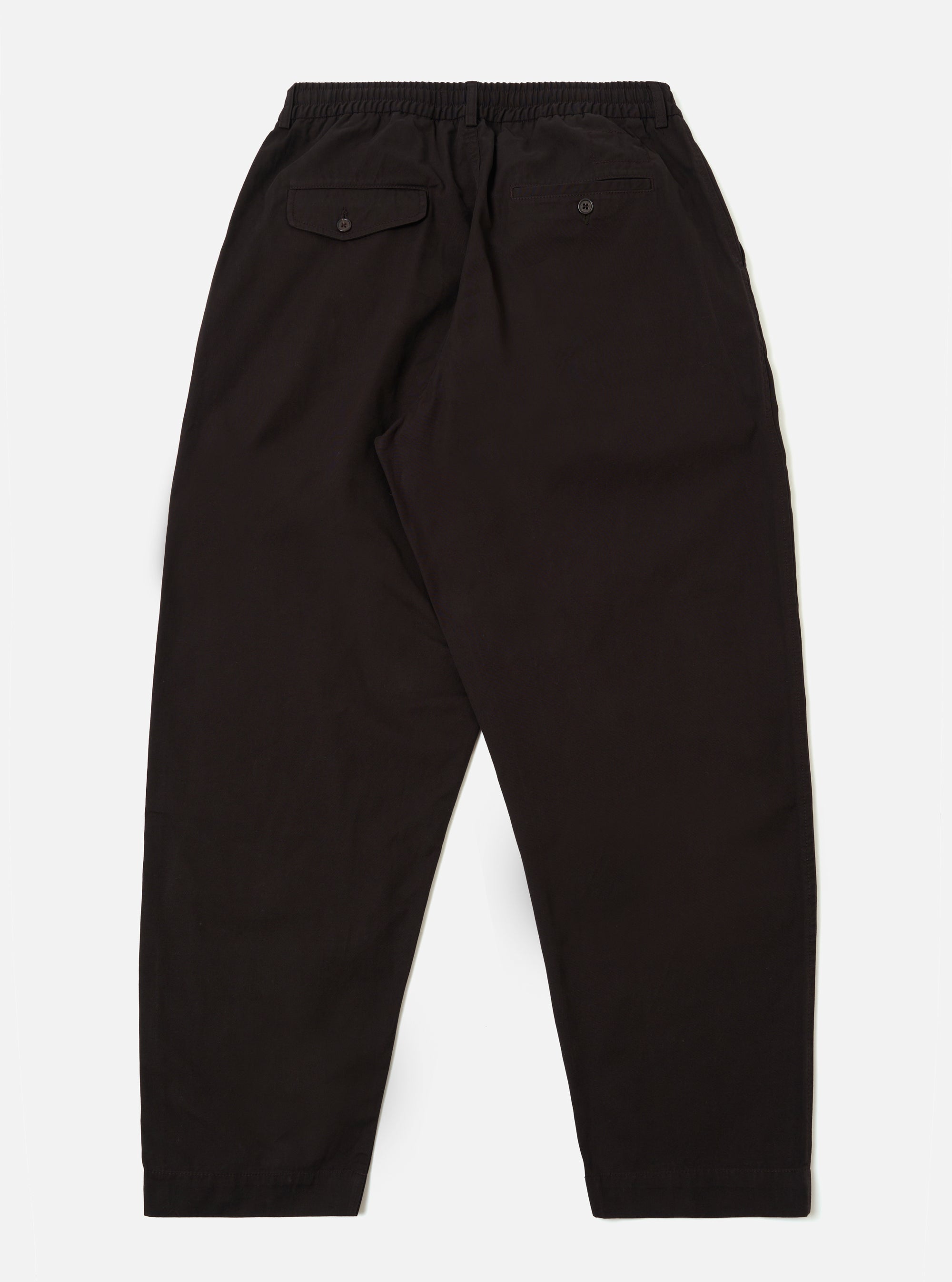 The Licorice Summer Canvas Pleated Track Pant is shown from a rear angle as a flat lay against a plain white background. The image highlights the single rear patch pocket with a buttoned flap and the elasticated waistband. The dark brown cotton canvas fabric features visible stitching details along the seams and hem.