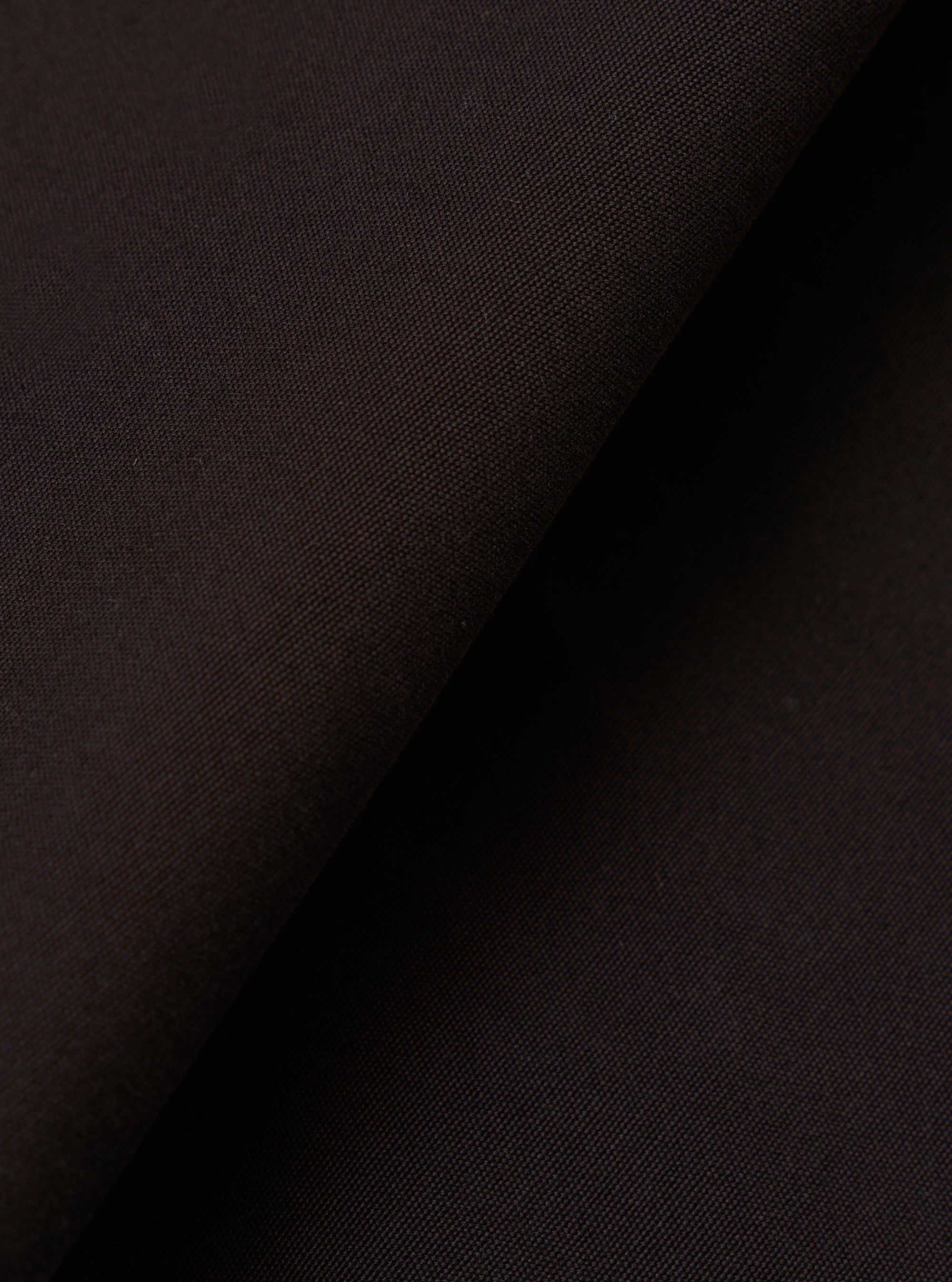 A close-up fabric swatch of the Licorice Summer Canvas Pleated Track Pant highlights the rich licorice brown color and the durable, textured weave of the summer canvas material. The fabric fills the entire frame.