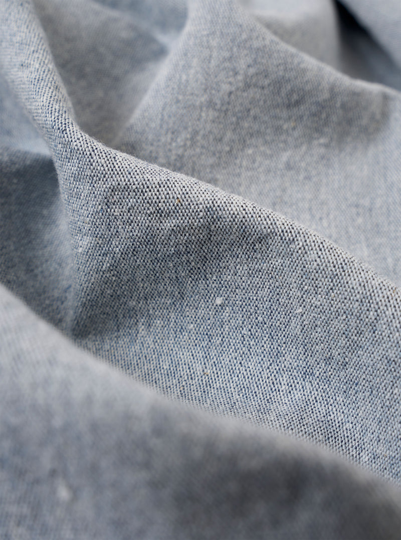 A close-up fabric swatch of the Light Indigo Jean Cloth Reworked Duke Pant highlights the light blue indigo-dyed organic cotton material. The image focuses on the textured weave of the fabric, filling the entire frame.
