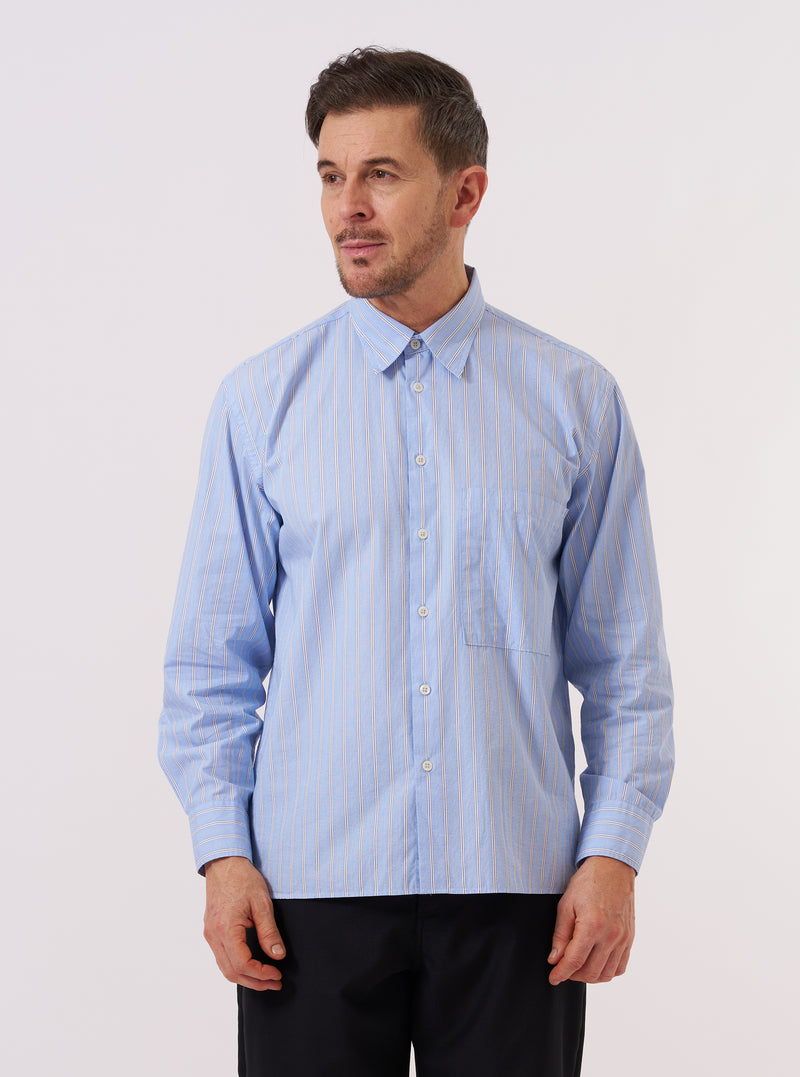 A model wears the Blue Mc Stripe Square Pocket Shirt against a plain, light grey background. The shirt features a blue and white vertical stripe pattern, a classic button-down front, a structured collar, and two large square patch pockets at the chest. The model is shown from a front-facing angle, wearing the shirt buttoned up with the sleeves down.