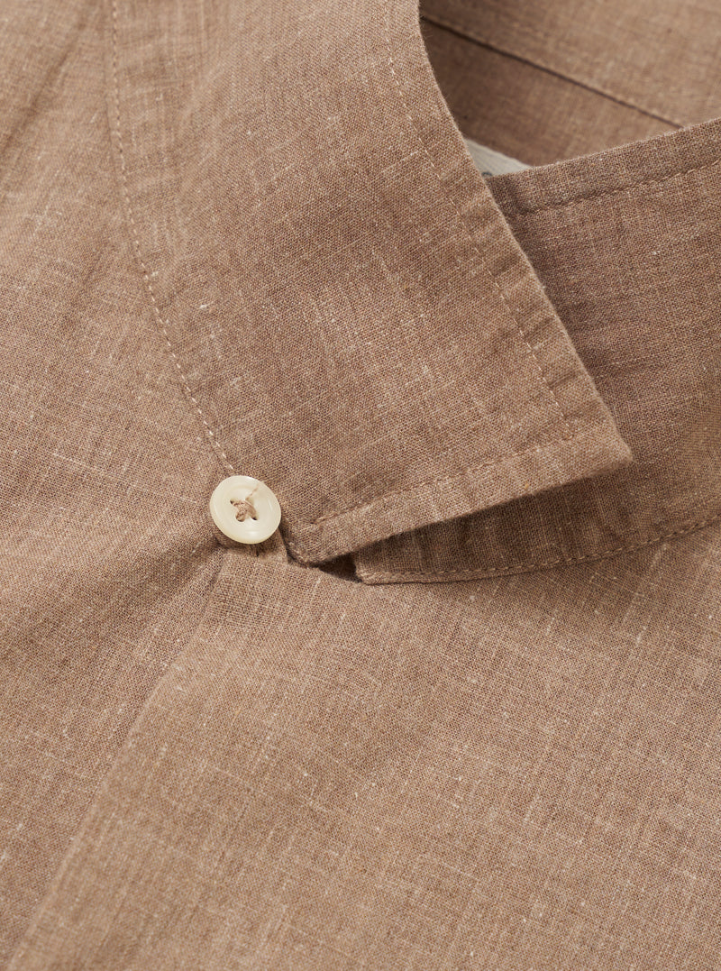 A model is wearing the Brown Sido Linen Mix Road Shirt, shown from the chest down against a plain white background. The shirt is unbuttoned over a white t-shirt, highlighting the camp collar, a single chest patch pocket, and a straight hem. The fabric has a textured linen-cotton weave and a subtle tonal pattern.