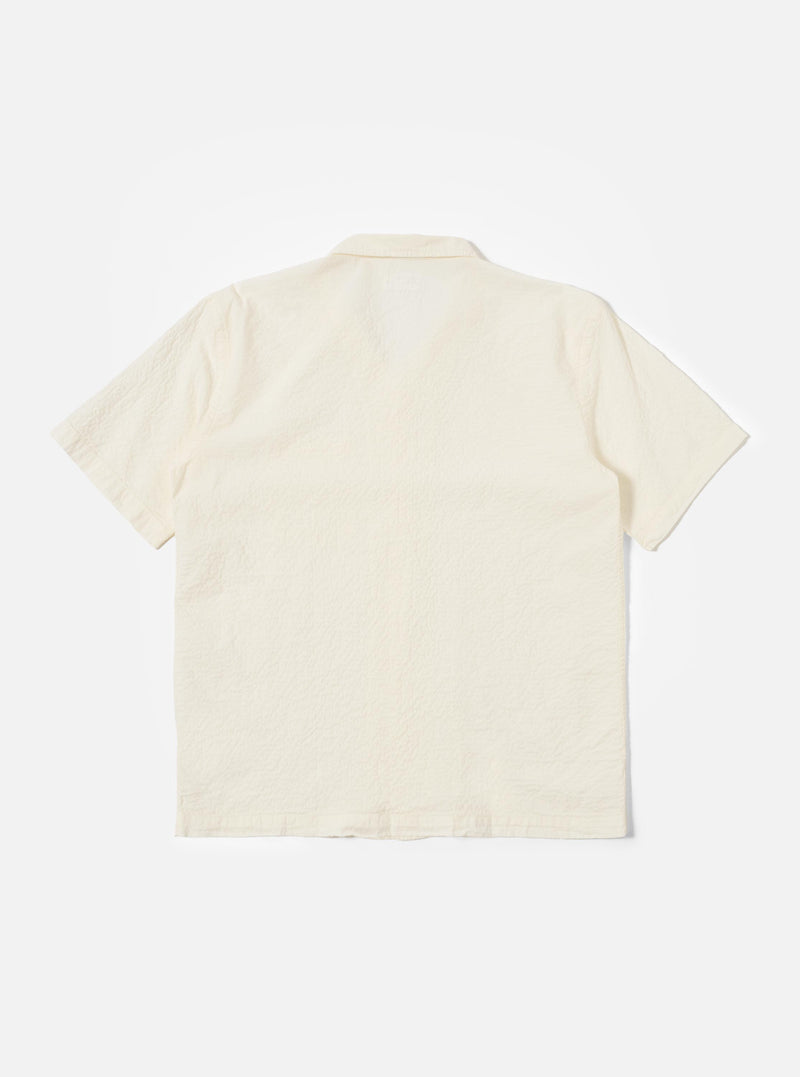 The Ecru Arten Seersucker Road Shirt is shown from the back as a flat lay against a plain white background. The image highlights the shirt's straight hem, short sleeves, and the distinct puckered texture of the ecru seersucker fabric. A clean horizontal yoke is visible across the shoulders.
