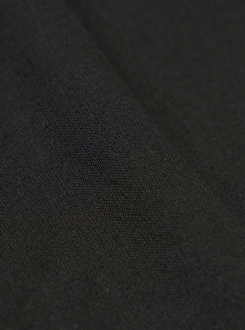 A close-up swatch image of the Black Valencia Cotton Pleated Track Pant fabric highlights the fine, plain weave and smooth texture of the black material. The fabric fills the entire frame, providing a detailed view of the lightweight suiting blend.