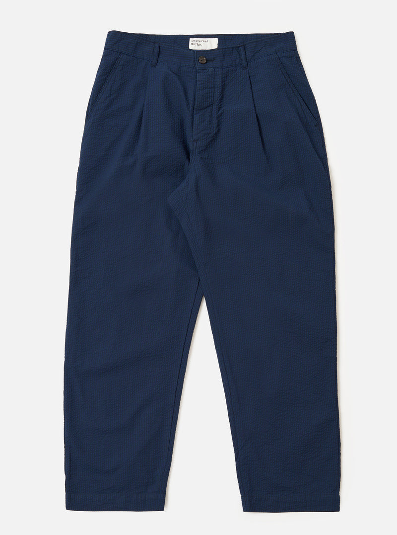 The Navy Derby Stripe Duke Pant is shown as a flat lay against a white background. These wide-leg trousers feature a dark navy cotton fabric with fine vertical derby stripes. The design includes a pleated front, a button fly, and two side pockets.
