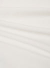 A close-up fabric swatch of the Ecru Organic Jersey Print Pocket Tee highlights the off-white ecru color and the fine, soft knit texture of the organic cotton jersey fabric. The material fills the frame, providing a detailed view of the textile's surface.