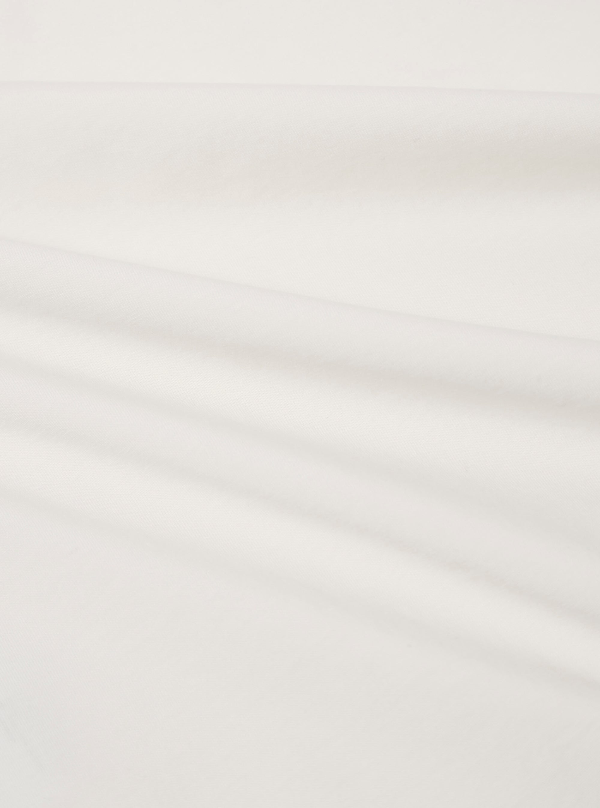 A close-up fabric swatch of the Ecru Organic Jersey Print Pocket Tee highlights the off-white ecru color and the fine, soft knit texture of the organic cotton jersey fabric. The material fills the frame, providing a detailed view of the textile's surface.