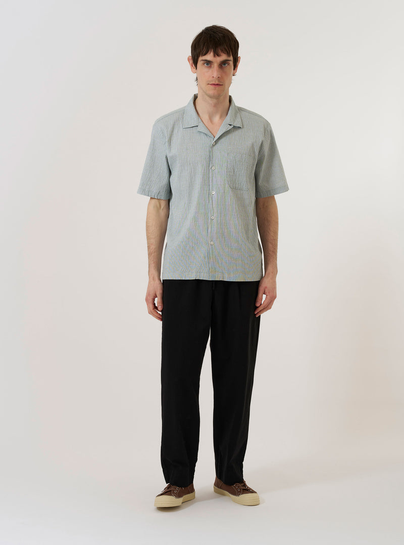 The Green Seersucker Road Shirt is shown as a flat lay against a plain white background. The shirt features a camp collar, a button-front closure, and a single chest patch pocket. The fabric has a distinct puckered seersucker texture in a solid green color.