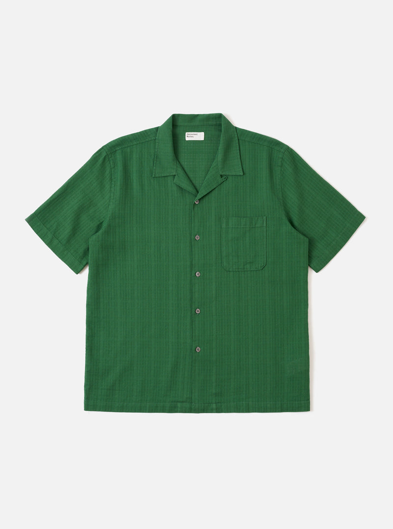 The Green Letts Cotton Road Shirt is presented as a flat lay against a plain white background. The shirt features a camp collar, a central button-down front, and a single patch pocket on the left chest. The short-sleeved garment is made from a solid green cotton fabric.