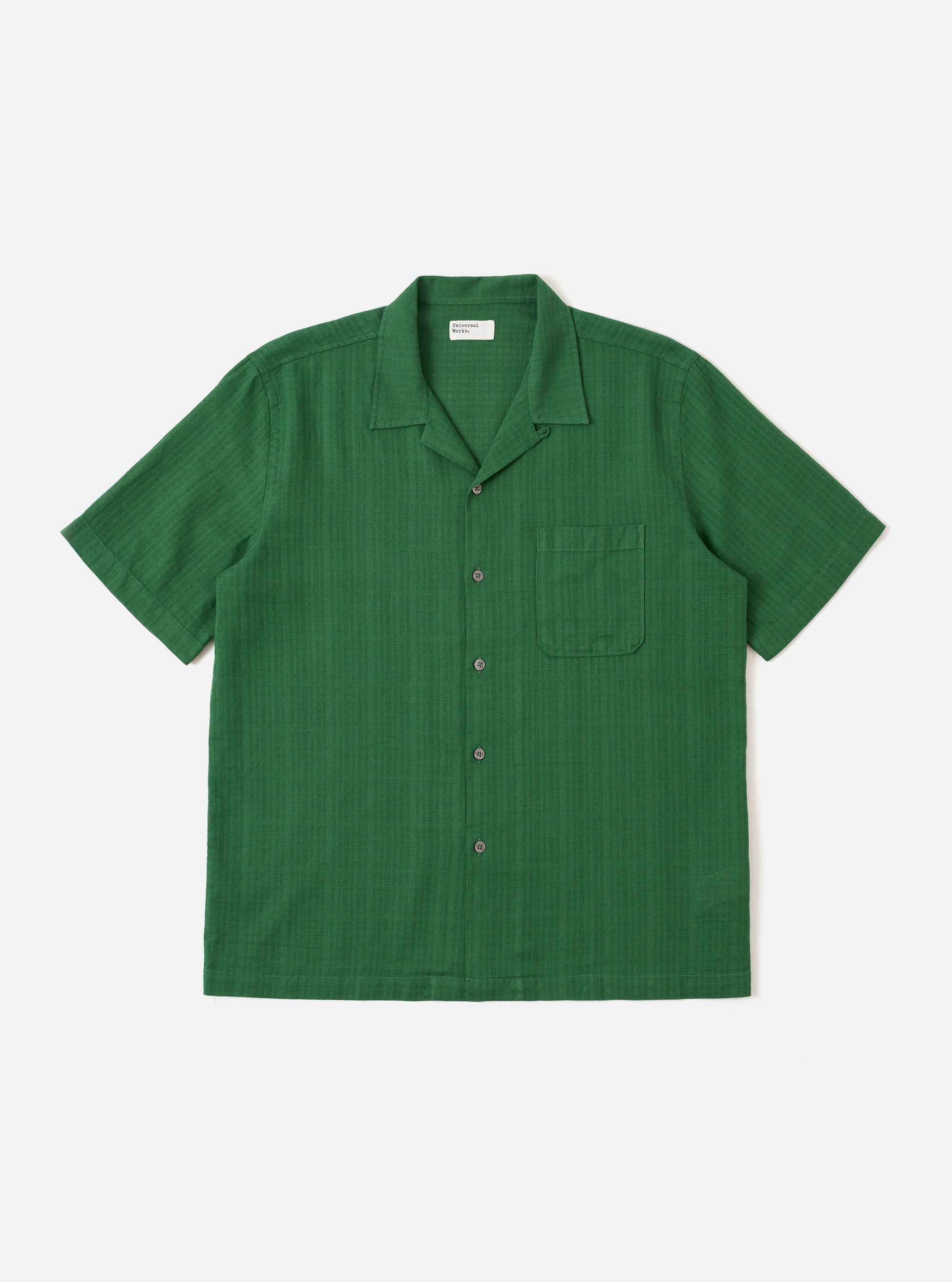 The Green Letts Cotton Road Shirt is presented as a flat lay against a plain white background. The shirt features a camp collar, a central button-down front, and a single patch pocket on the left chest. The short-sleeved garment is made from a solid green cotton fabric.