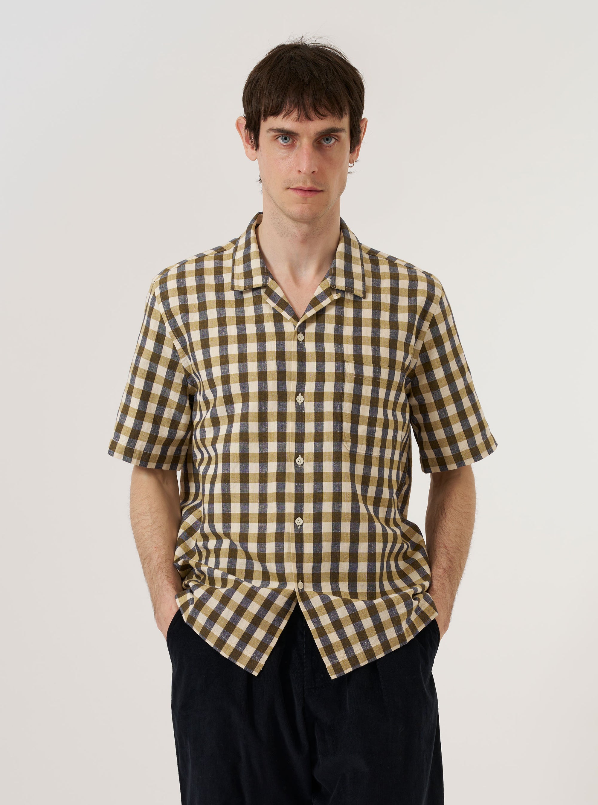 A model wears the Olive Aberdeen Lincot Road Shirt over a white T-shirt against a plain white background. The shirt features a relaxed fit, a camp collar, and a central button-down closure. The olive green fabric is a cotton and linen blend with a subtle textured appearance.