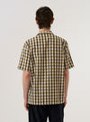 A model wears the Olive Aberdeen Lincot Road Shirt against a plain white background, shown from the back. The shirt features a relaxed fit, a straight hem, and a simple back yoke. The olive green fabric, a blend of cotton and linen, has a visible textured weave. The model is wearing the shirt untucked over dark trousers.