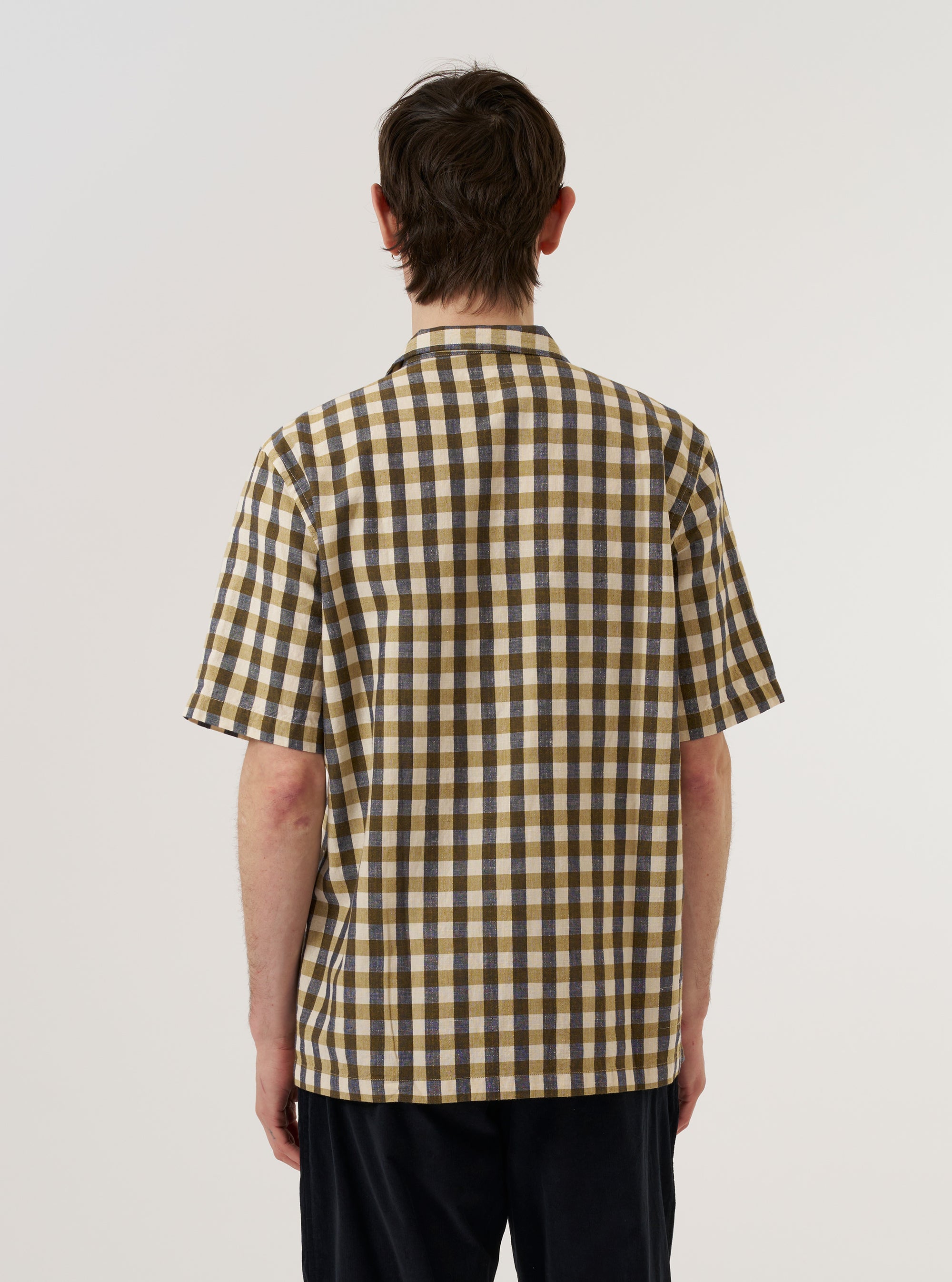 A model wears the Olive Aberdeen Lincot Road Shirt against a plain white background, shown from the back. The shirt features a relaxed fit, a straight hem, and a simple back yoke. The olive green fabric, a blend of cotton and linen, has a visible textured weave. The model is wearing the shirt untucked over dark trousers.