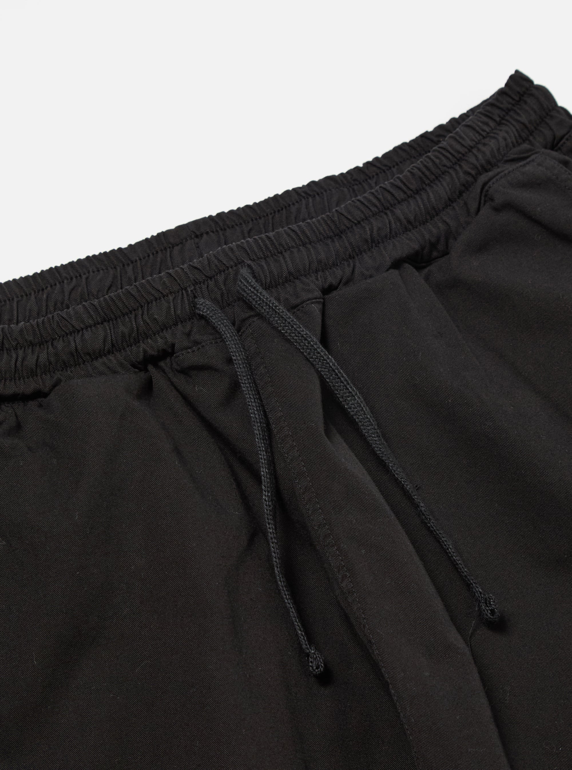 The Black Kelly Cotton Simple Short is shown from the back as a flat lay against a plain white background. The shorts feature an elasticated waistband and a single patch pocket on the right rear side. The fabric is a solid black cotton with visible stitching details.