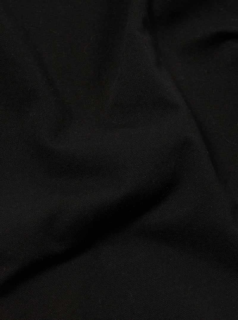 A close-up fabric swatch of the Black Kelly Cotton Simple Short highlights the solid black color and the smooth, fine texture of the cotton material. The fabric fills the frame, providing a detailed view of the weave and finish.
