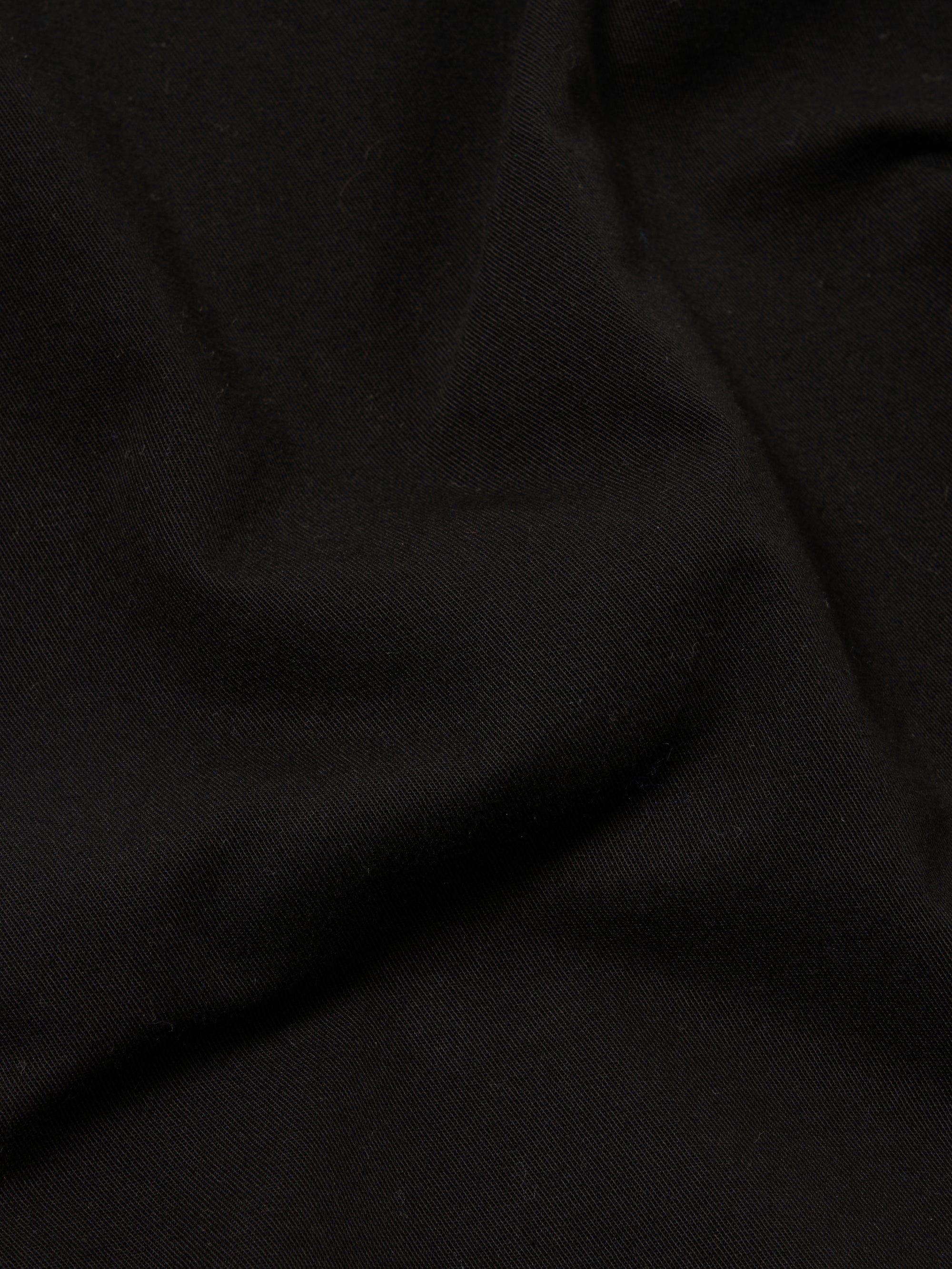 A close-up fabric swatch of the Black Kelly Cotton Simple Short highlights the solid black color and the smooth, fine texture of the cotton material. The fabric fills the frame, providing a detailed view of the weave and finish.