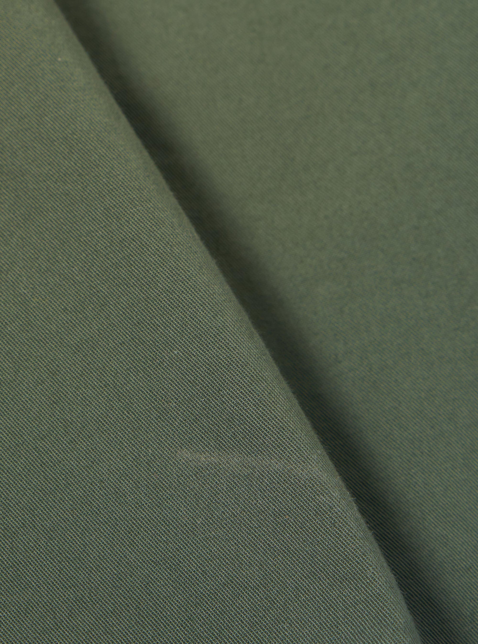 A close-up swatch image of the Olive Kelly Cotton Simple Short fabric highlights the olive green color and the subtle, woven texture of the kelly cotton material. The fabric fills the frame, providing a detailed view of the garment's color and construction.