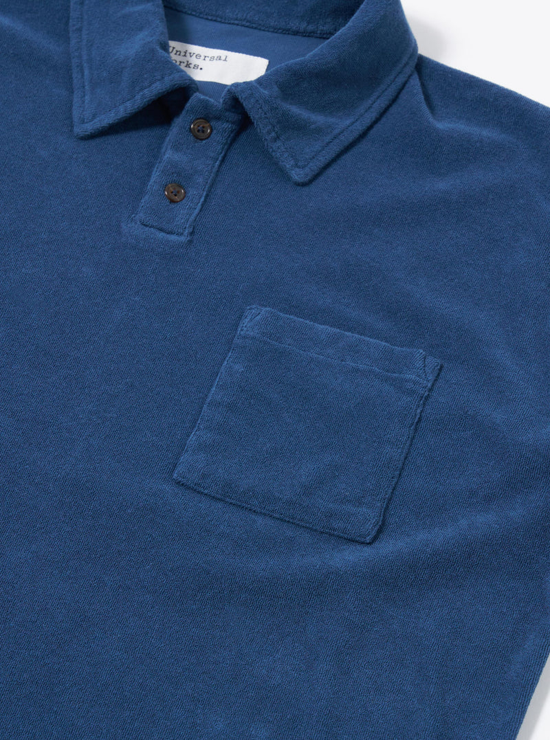 The Navy Light Weight Terry Newlyn Polo is displayed from the back as a flat lay against a plain white background. The image highlights the simple one-piece collar, the straight hem with side splits, and the soft texture of the navy blue light weight terry fabric.