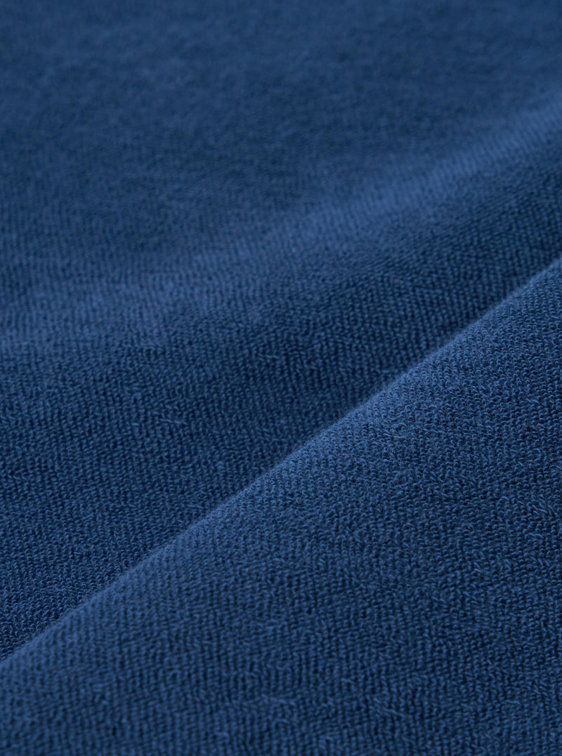 A close-up swatch image of the Navy Light Weight Terry Newlyn Polo fabric displays a deep navy blue color with a soft, looped terry cloth texture. The material is shown as a detailed textile sample against a neutral background.