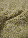 A close-up fabric swatch of the Light Olive Alvar Fleece Lancaster Gilet highlights the thick, curly texture of the light olive green fleece material. The textured wool-blend fabric fills the frame, providing a detailed view of the garment's color and looped weave.