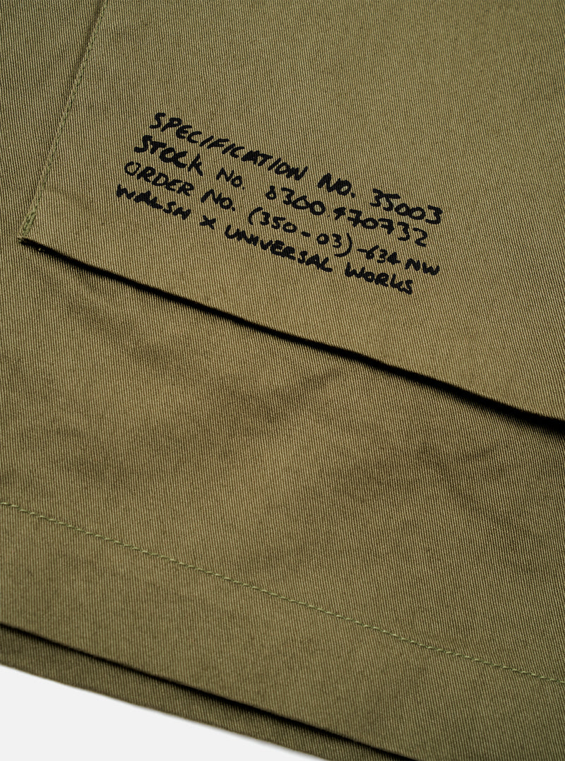 Rear view of a model wearing the Walsh x Universal Works Light Olive Twill Troopers Jacket against a plain studio background. The image displays the clean back panel construction, straight hem cut, and comfortable overshirt fit.