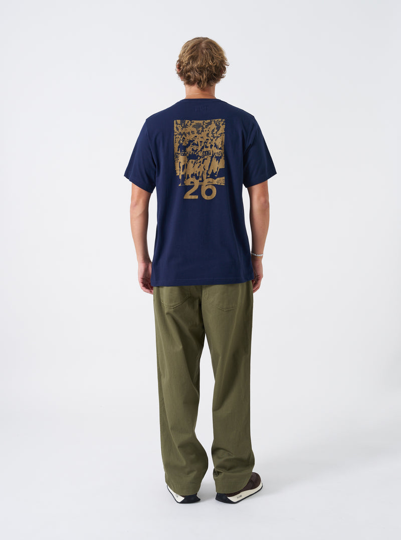 A model presents the Walsh x Universal Works Navy Single Jersey T Shirt against a plain studio background. The alternative view focuses on the relaxed fit across the chest, shoulders, tidy hemline, and deep navy colorway.