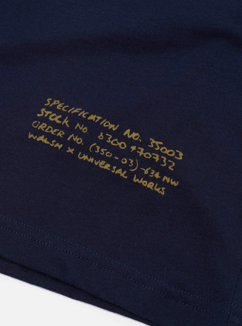 A close-up view of the collar and print detail on the Walsh x Universal Works Navy Single Jersey T Shirt against a neutral background. The image emphasizes the fine ribbing, collar construction, logo graphics, and navy cotton fabric.
