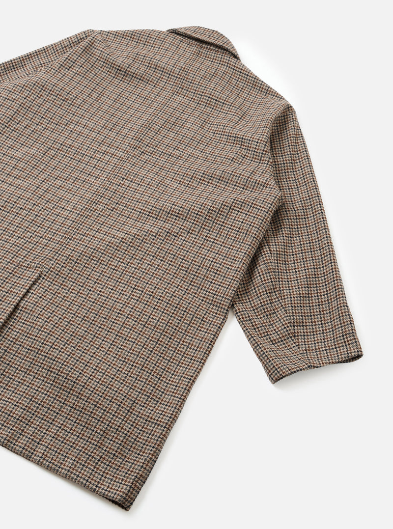An angled product shot of the Taupe Lester Dogtooth Stan Coat set against a clean neutral background. Prominent features include the structured overcoat silhouette, woven dogtooth check pattern, and deep side pockets.