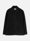 Black wool-texture Mowbray heavy duty jacket laid flat on a light grey studio backdrop. Point collar, four-button front fastening, one chest patch pocket with flap, two large lower flap pockets, and long sleeves with plain cuffs. Universal Works woven label visible at the collar.