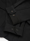 Close-up detail of the black Mowbray heavy duty jacket laid flat on a white surface. The shot focuses on the button placket and cuffs, showing dark four-hole buttons on a structured front placket and buttoned barrel cuffs. The fabric is a dense, matte wool-blend with a lightly brushed texture.