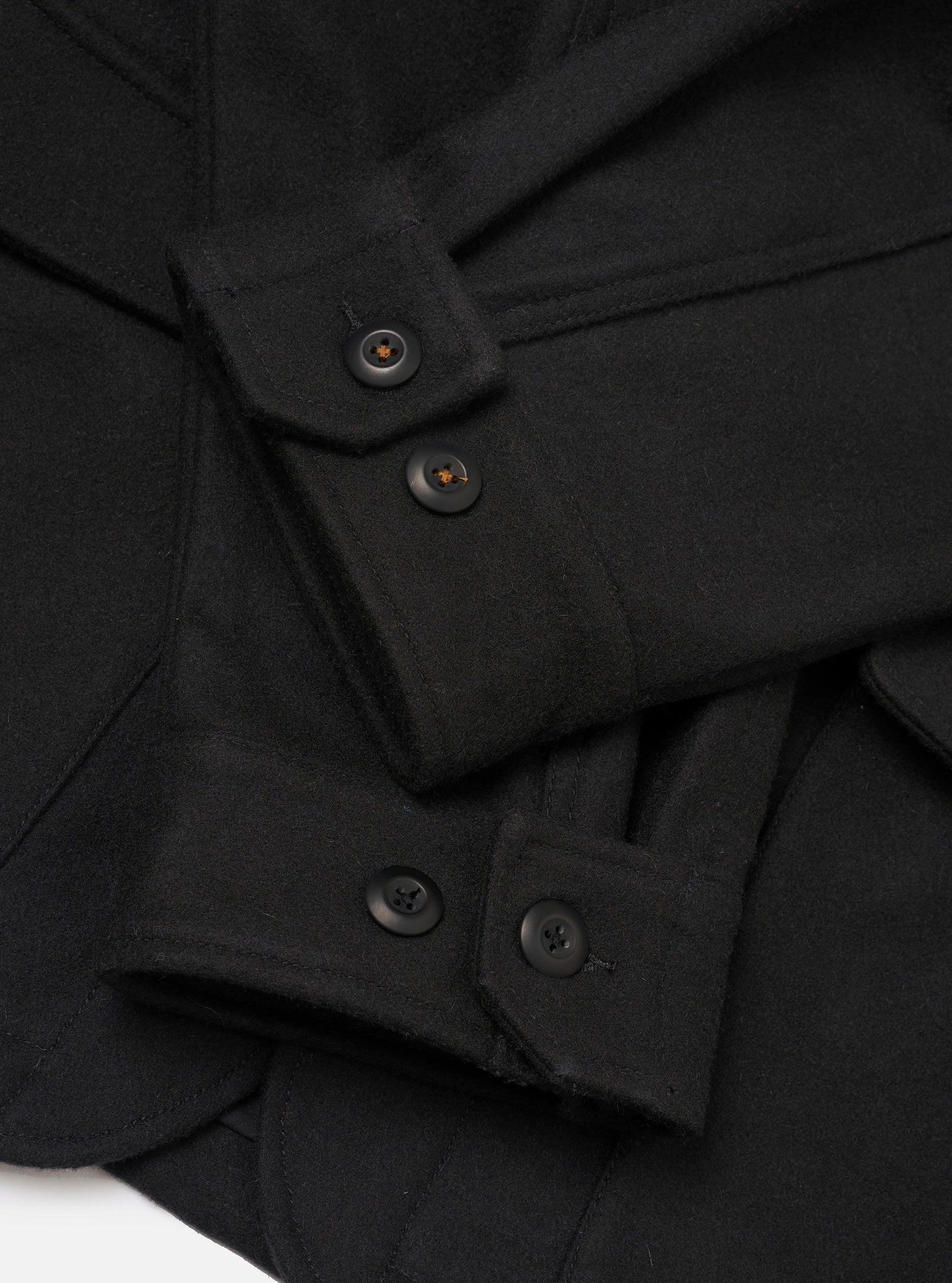 Close-up detail of the black Mowbray heavy duty jacket laid flat on a white surface. The shot focuses on the button placket and cuffs, showing dark four-hole buttons on a structured front placket and buttoned barrel cuffs. The fabric is a dense, matte wool-blend with a lightly brushed texture.