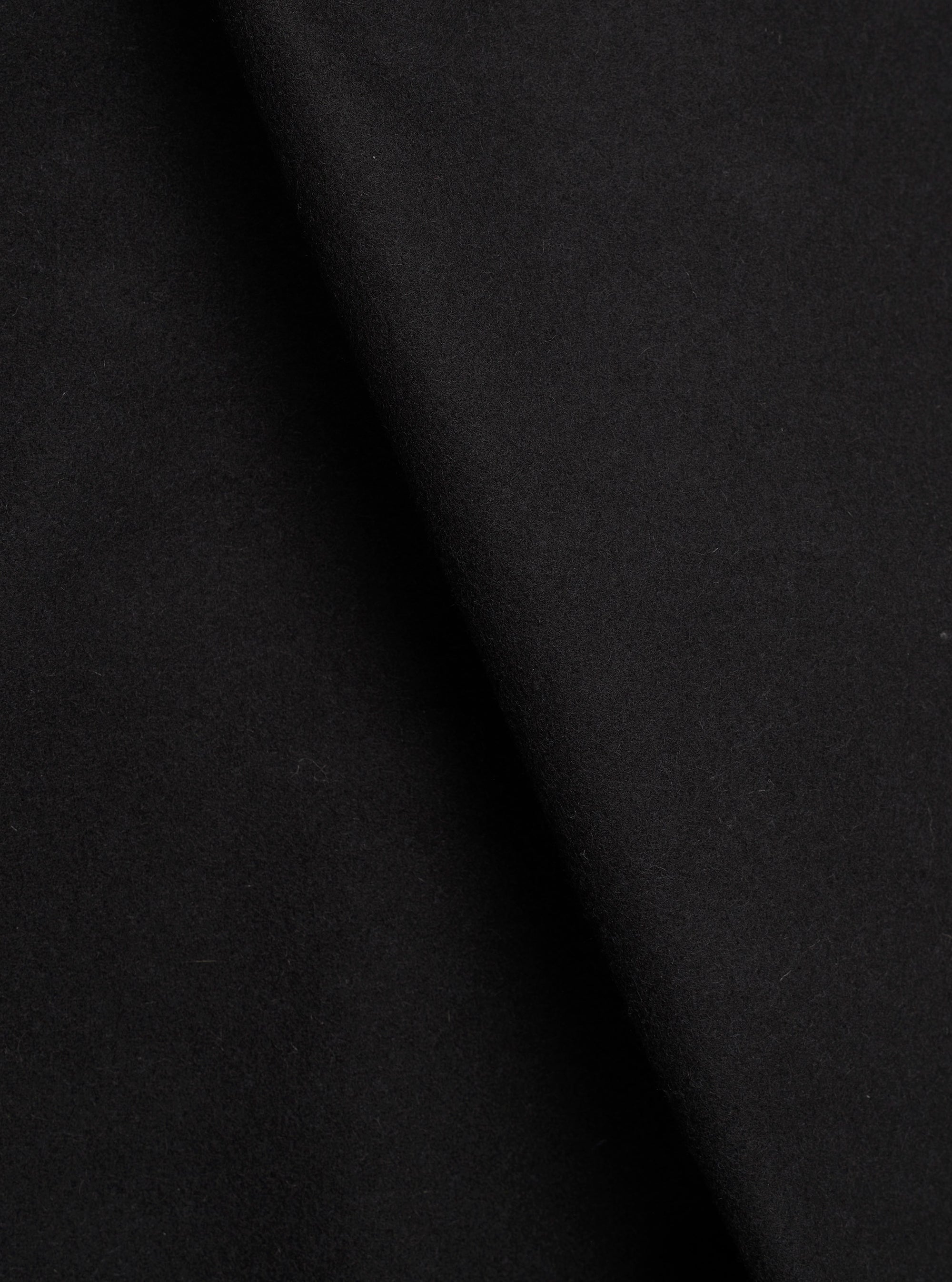 Close-up of the black Mowbray Heavy Duty Jacket fabric, showing a soft, dense wool-like texture with a matte finish. The material is draped with gentle folds creating subtle shadow variation across the surface. No garment details or background are visible in this tight fabric shot.