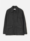 Grey marl wool chore jacket laid flat on a light grey seamless backdrop. Point collar with a Universal Works woven label at the neck. Four button front placket with dark buttons. Two chest patch pockets and two large flap pockets at the hem. Long sleeves with plain cuffs. Brushed, lightly flecked wool fabric throughout.