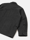 Flat lay of the grey marl heavy duty jacket on a white surface, shot from above at an angle showing the back and right sleeve. The melange wool fabric has a dense, felted texture. A yoke seam runs across the upper back. The cuff features two dark buttons, and a welt pocket is visible on the sleeve.