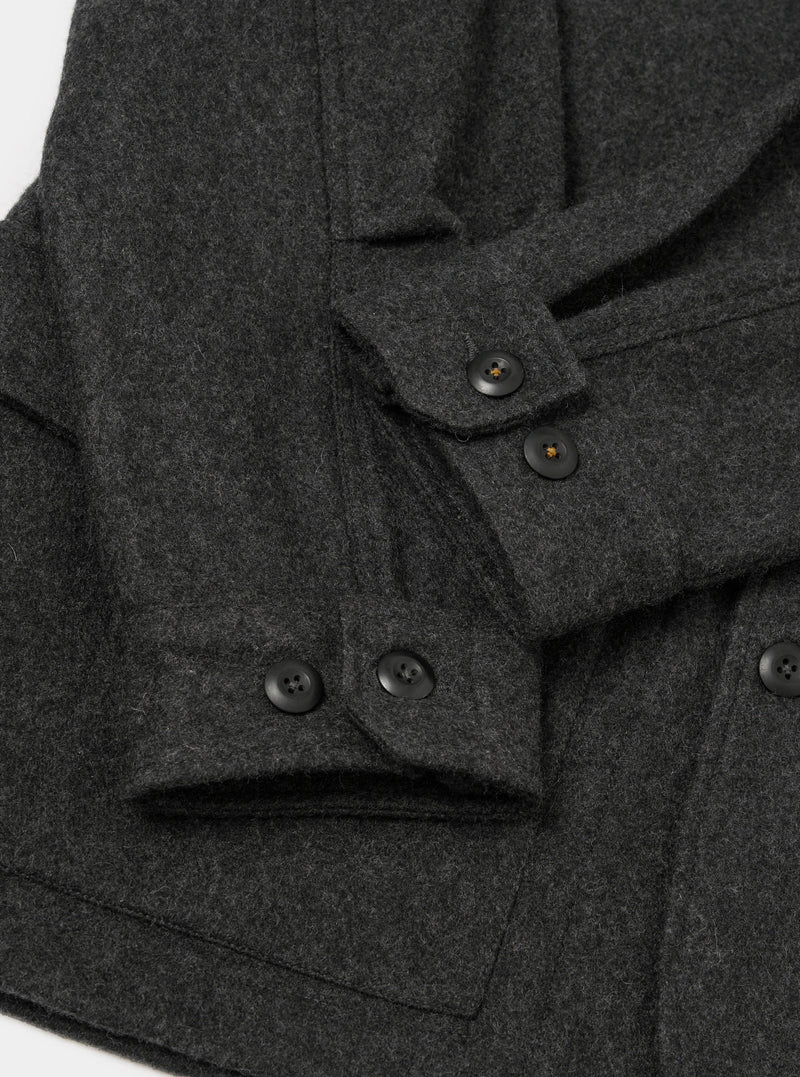Close-up flat lay of the grey marl Mowbray heavy duty jacket on a white surface. The brushed wool fabric has a dense, textured marl finish. Four-hole black buttons are visible on two button cuffs and along the front placket. A patch pocket is visible at the lower left.