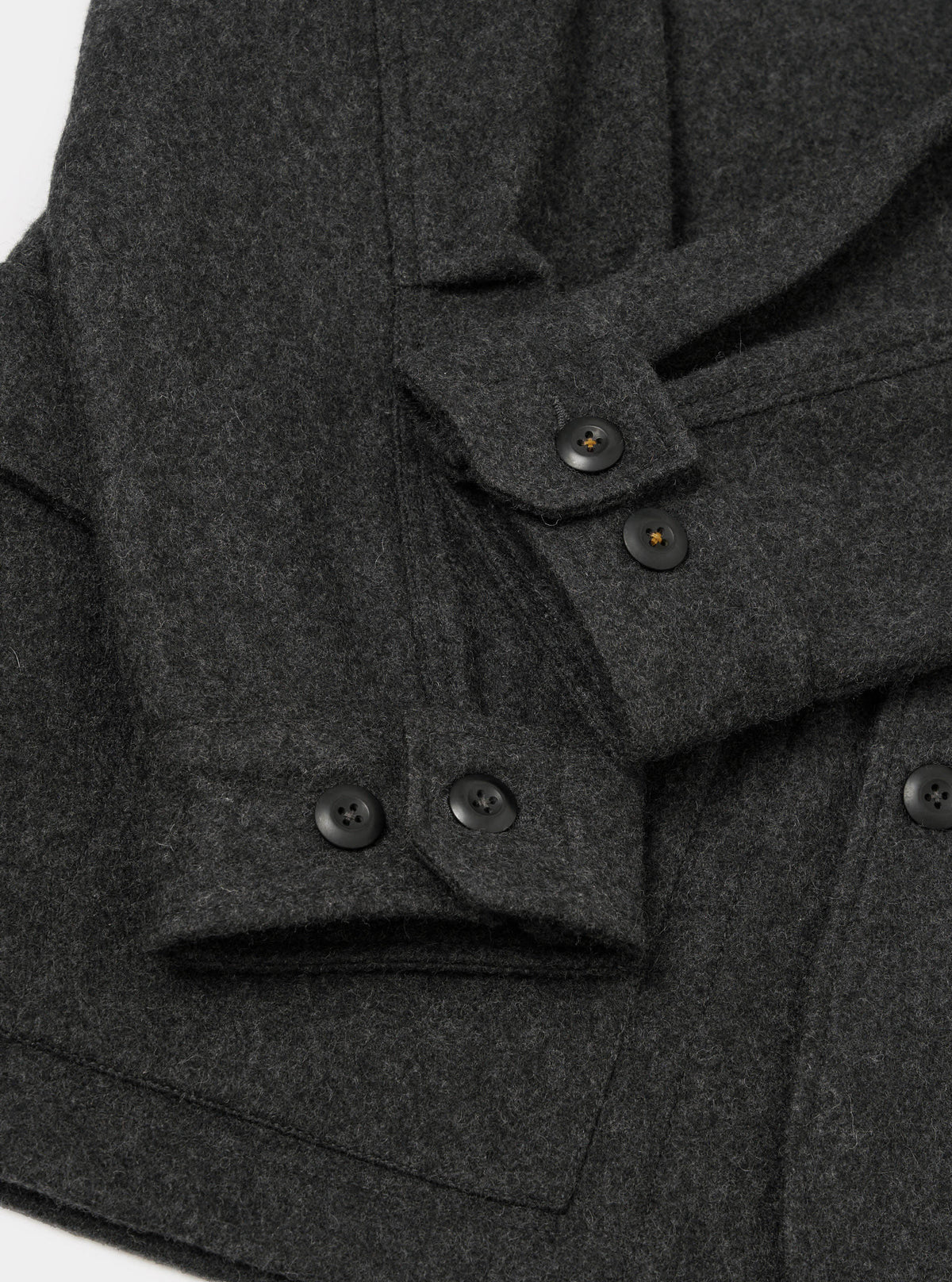 Close-up flat lay of the grey marl Mowbray heavy duty jacket on a white surface. The brushed wool fabric has a dense, textured marl finish. Four-hole black buttons are visible on two button cuffs and along the front placket. A patch pocket is visible at the lower left.