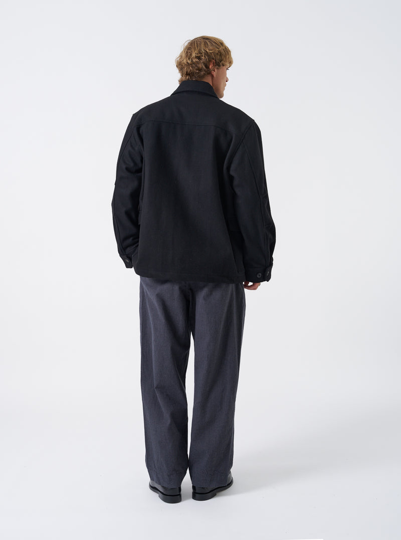 A male model stands against a neutral studio backdrop wearing the Black Mowbray Heavy Duty Jacket. The shot displays the back profile, heavy wool-blend texture, comfortable fit, and clean shoulder seams.