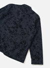 Black wool-mix chore jacket in a bakers cut, laid flat on a white surface, shot from a rear three-quarter angle. The fabric features a tonal abstract floral jacquard pattern in black on navy. A small collar, rear seam, curved hem, and plain long sleeve cuff are visible.