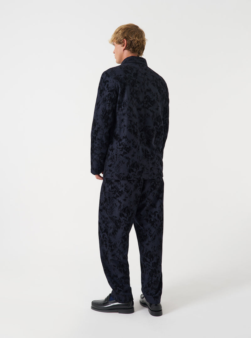 A model poses in a studio setting against a light backdrop wearing the Black Be Bop Wool Mix OG Bakers Chore Jacket. The photograph displays the fit, structured shoulders, buttoned placket, and deep utility pockets.
