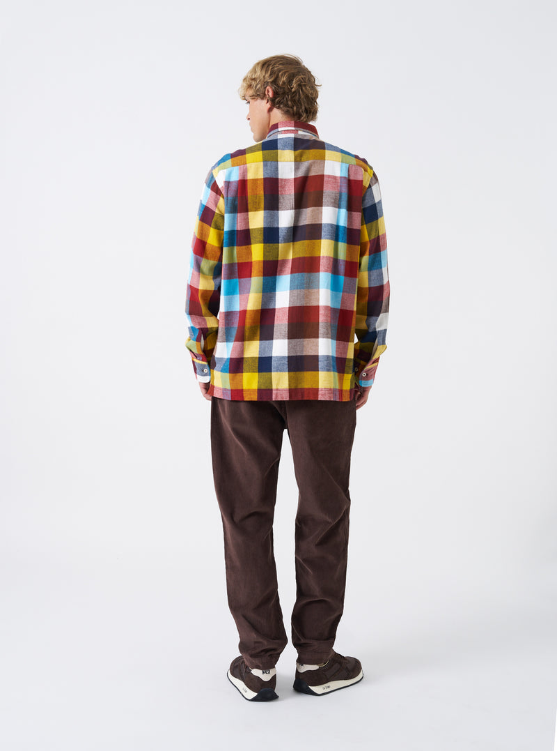 A male model stands against a plain neutral background wearing the Multi Check Evans Check Lucky Shirt. The image highlights the colorful check pattern, buttoned front, classic collar, and relaxed fit of the long-sleeved shirt.
