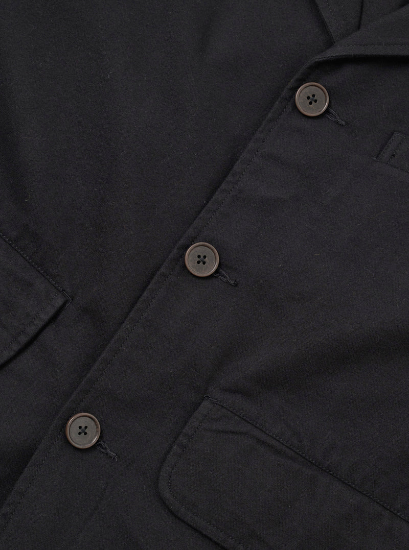 Close-up flat lay of the black brushed moleskin Franck jacket, showing the single-breasted button placket with three four-hole dark horn-effect buttons on a loophole fastening. Two patch pockets are visible at the lower chest and hip. The soft, dense fabric texture is prominent throughout. White studio background.