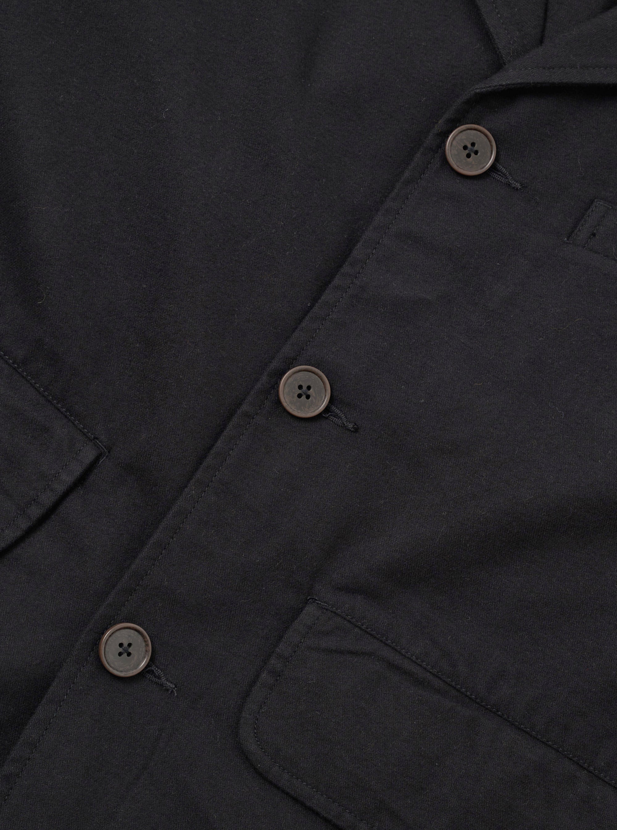 Close-up flat lay of the black brushed moleskin Franck jacket, showing the single-breasted button placket with three four-hole dark horn-effect buttons on a loophole fastening. Two patch pockets are visible at the lower chest and hip. The soft, dense fabric texture is prominent throughout. White studio background.