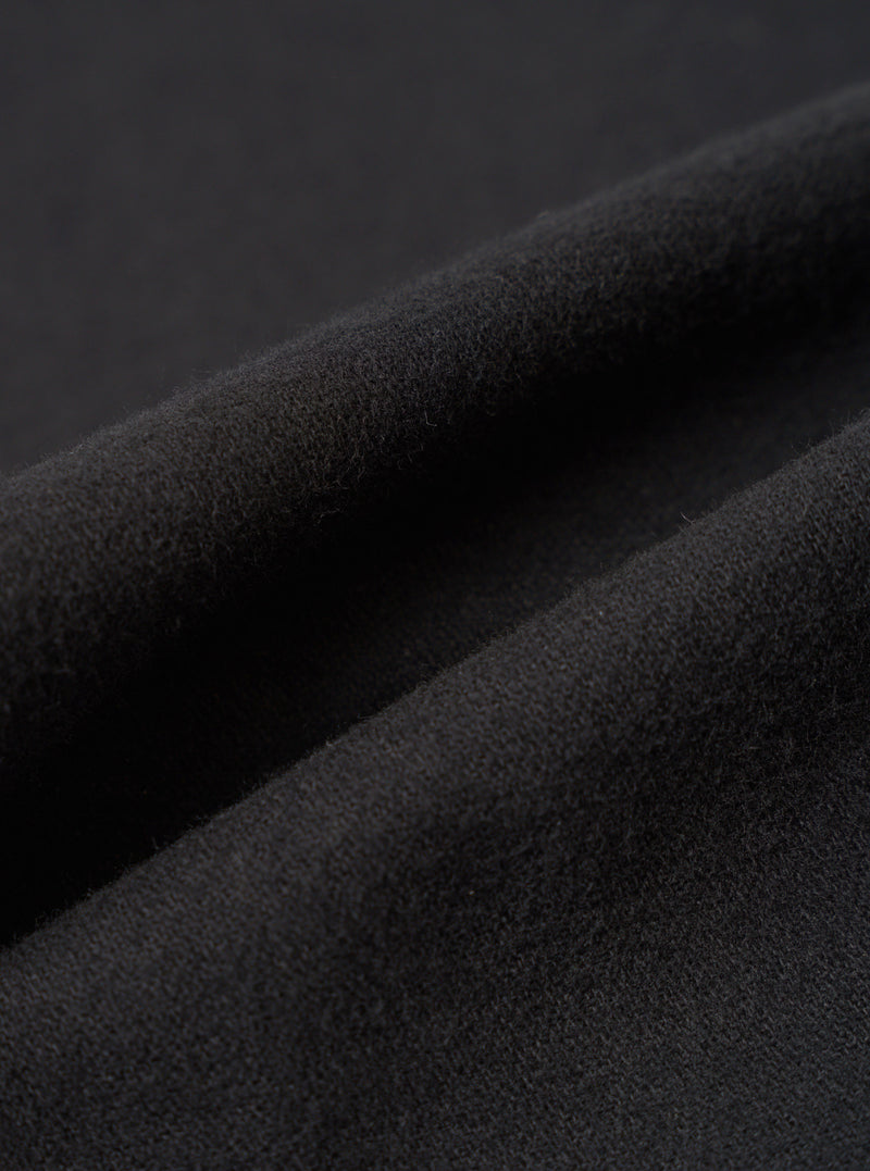 Close-up detail shot of the black brushed moleskin fabric used in the Franck Jacket. The macro image shows the dense, softly napped surface texture with gentle folds and ridges catching light to reveal the fabric's plush, fine-knit pile. Dark grey background.