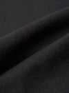 Close-up detail shot of the black brushed moleskin fabric used in the Franck Jacket. The macro image shows the dense, softly napped surface texture with gentle folds and ridges catching light to reveal the fabric's plush, fine-knit pile. Dark grey background.