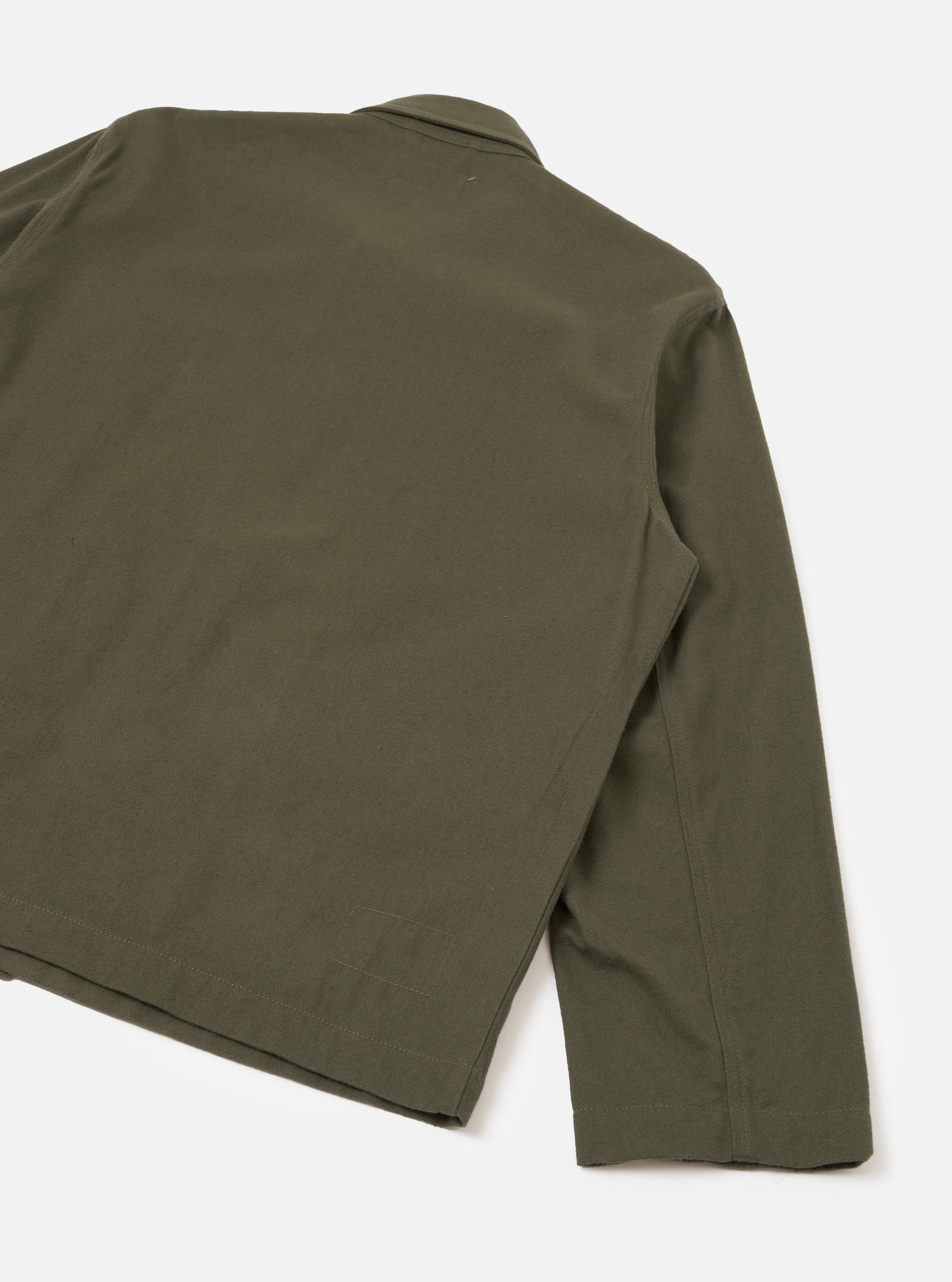 Close-up of the back and right sleeve of an olive brushed moleskin Franck jacket, laid flat on a white studio surface. The smooth, matte fabric shows a plain weave with no visible pattern. A shirt collar is partially visible at the top, and a topstitched hem runs along the bottom edge.