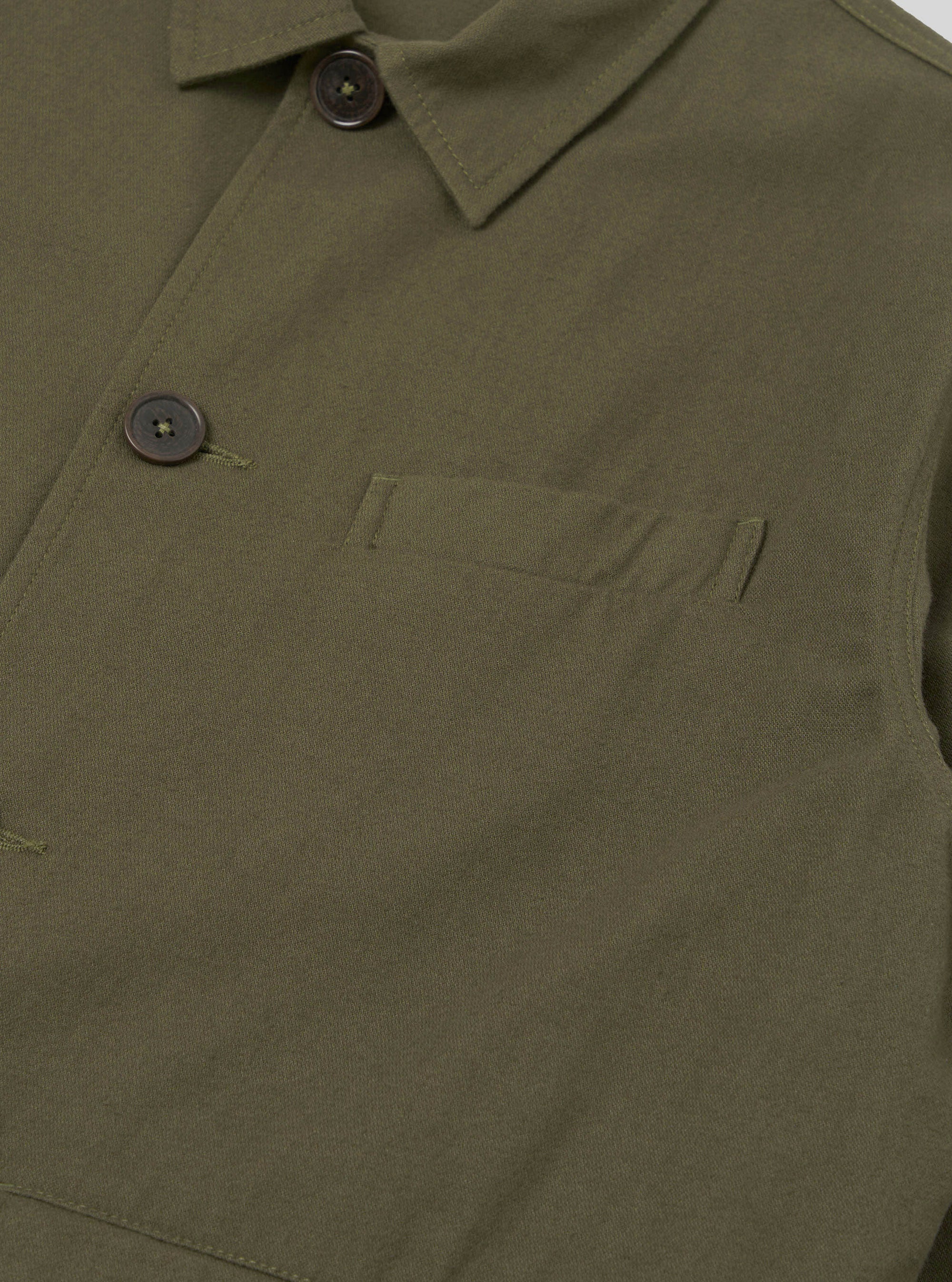 Close-up detail of the olive brushed moleskin Franck jacket on a plain white studio backdrop. The point collar, dark horn button at the neck, and a second button on the left chest placket are visible. A welt chest pocket with bartack stitching sits on the front body. The fabric has a smooth, dense texture.