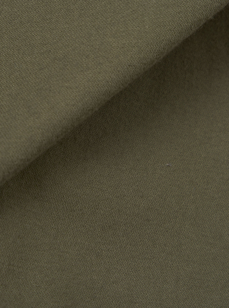Close-up of olive brushed moleskin fabric used in the Franck Jacket. The folded edge runs diagonally across the frame, showing the soft, lightly napped texture of the outer face against the smoother reverse side. Plain solid colour with no pattern or surface detailing visible.