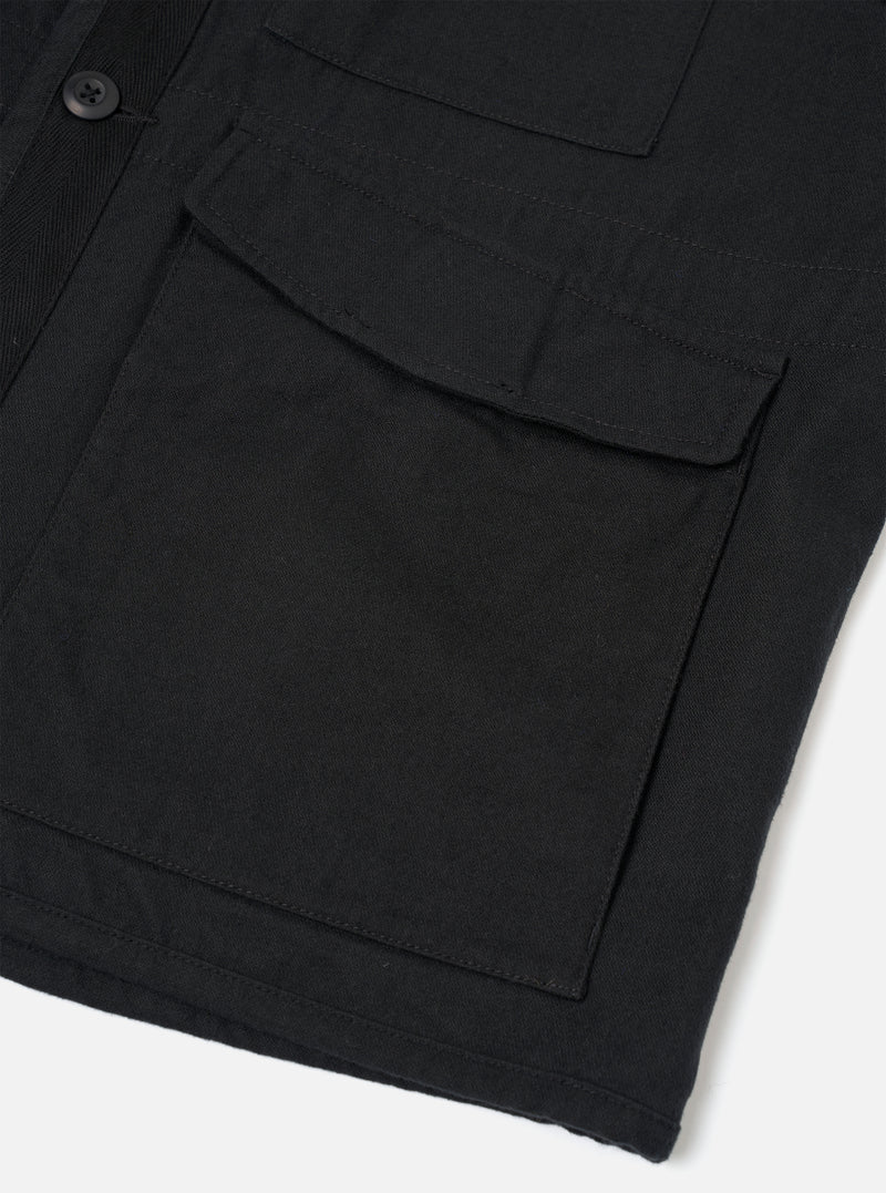 Close-up detail of a black brushed moleskin gilet, shot flat on a white surface. The image focuses on the front left section, showing a large flap patch pocket with topstitching and a smaller chest pocket above it. A single dark button is visible on the placket. The dense, matte fabric texture is clearly visible.