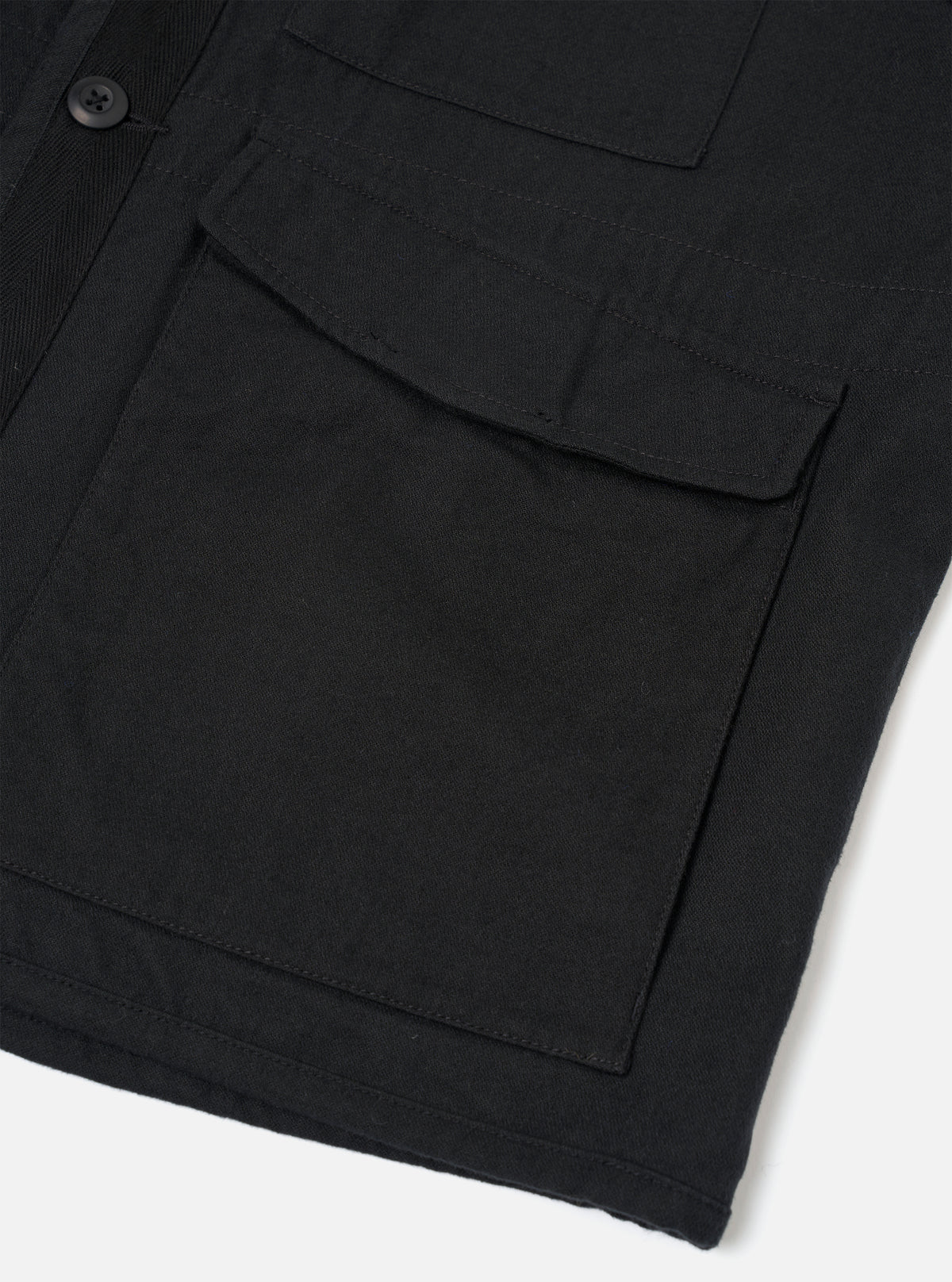 Close-up detail of a black brushed moleskin gilet, shot flat on a white surface. The image focuses on the front left section, showing a large flap patch pocket with topstitching and a smaller chest pocket above it. A single dark button is visible on the placket. The dense, matte fabric texture is clearly visible.
