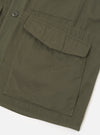 Close-up detail of an olive brushed moleskin gilet on a white studio backdrop. The shot shows two large flap patch pockets with contrast topstitching, a dark four-hole button visible at the front placket, and a herringbone-weave strap detail to the left side. The plain-weave fabric has a fine, dense texture.